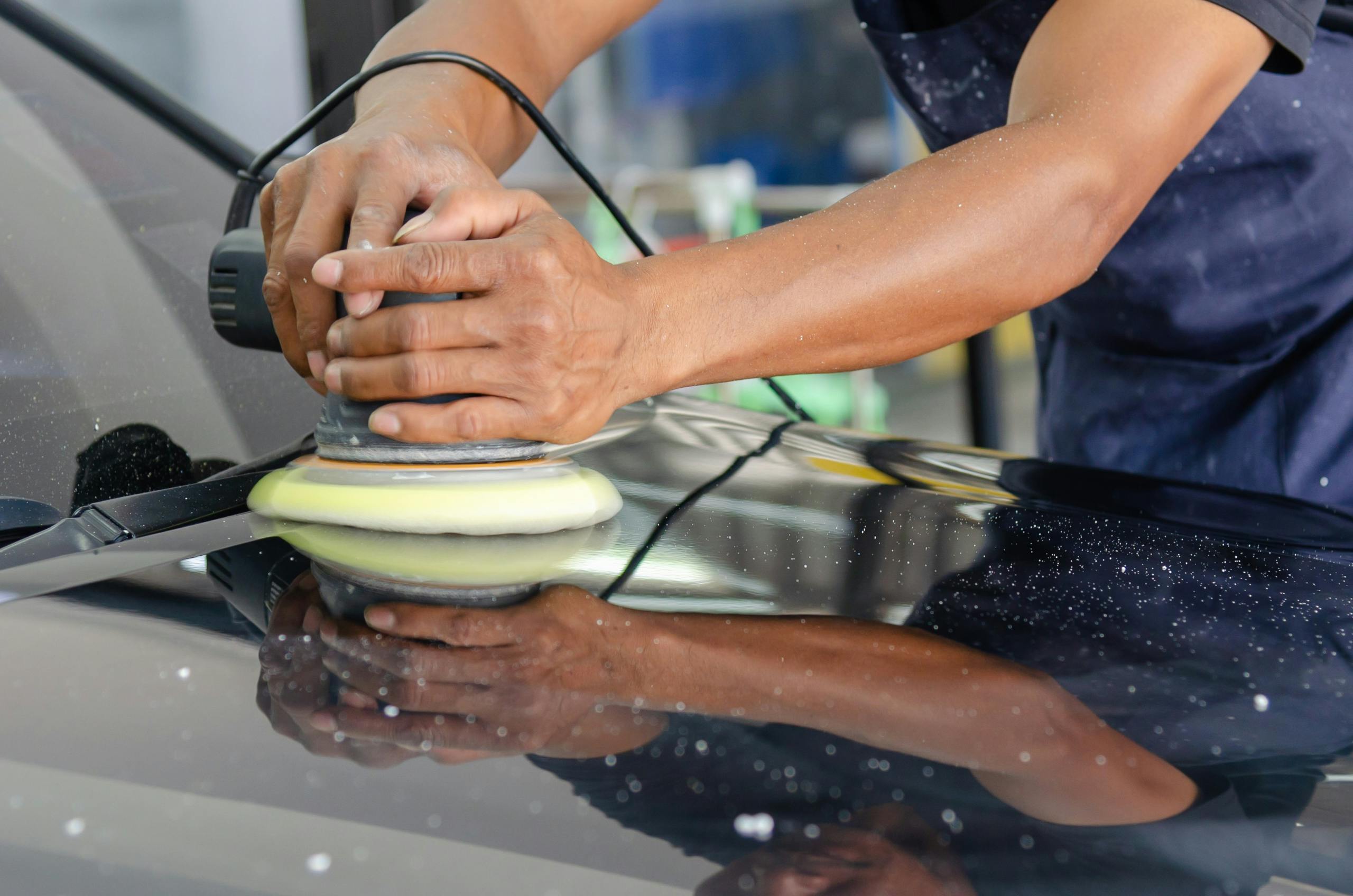 person using a car buffer to polish a black vehicle